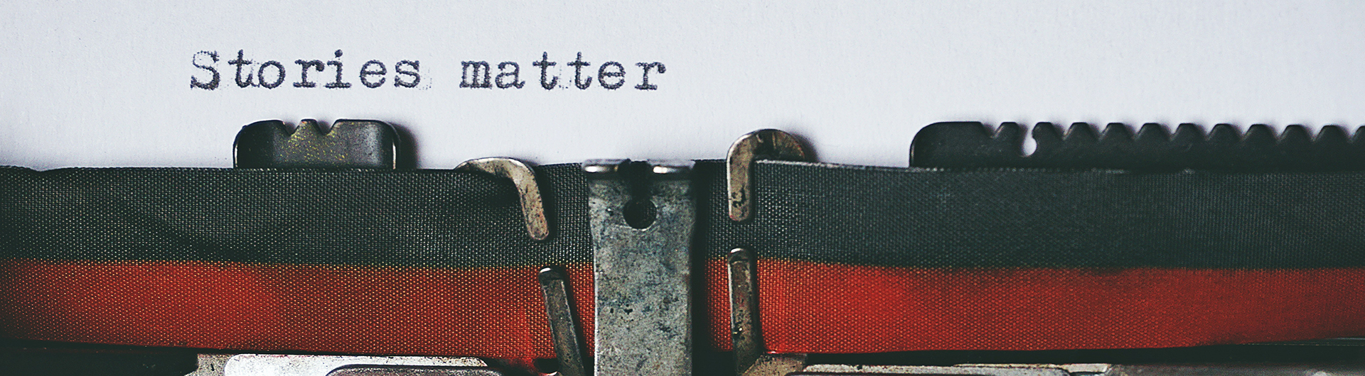 "Stories matter" freshly typed on white paper above a typewriter ribbon